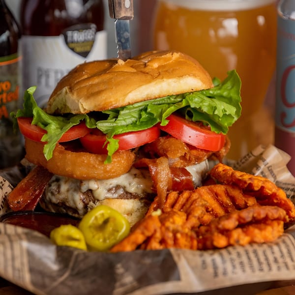 A loaded burger with onion rings, bacon, lettuce, tomato, and sweet potato fries.