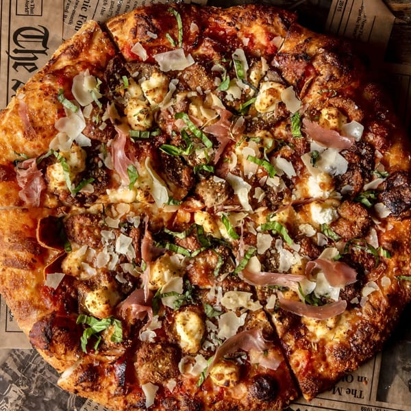 A Ginny's pizza with prosciutto, ricotta, basil, and parmesan, served on newspaper.