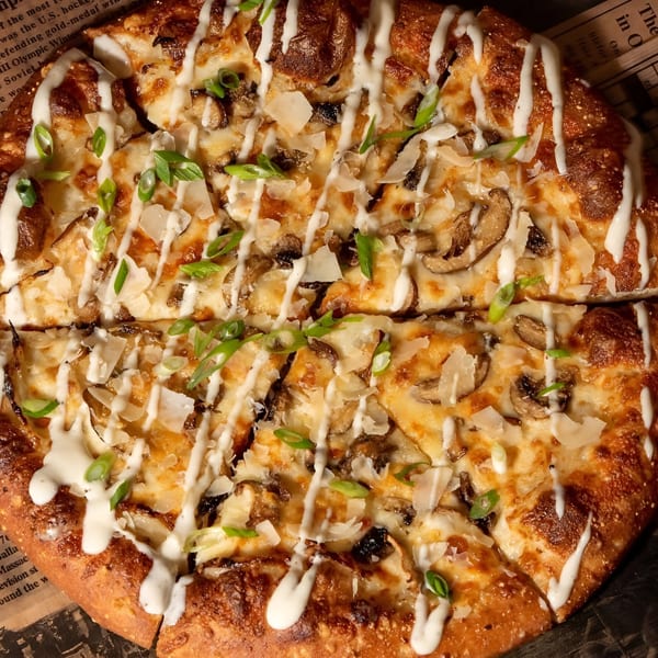 Ginny's mushroom pizza with white sauce drizzle, shaved cheese, and green onions.