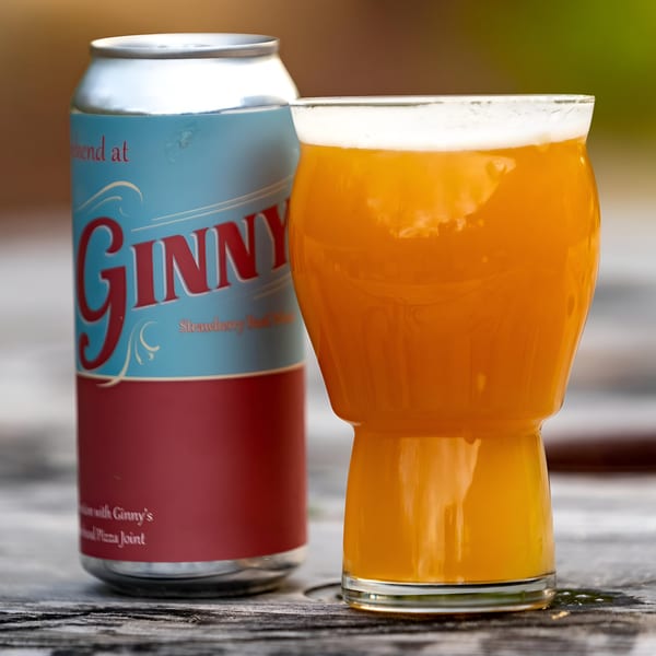 A Ginny's Strawberry Basil Wheat beer can next to a glass of the golden-orange beer.